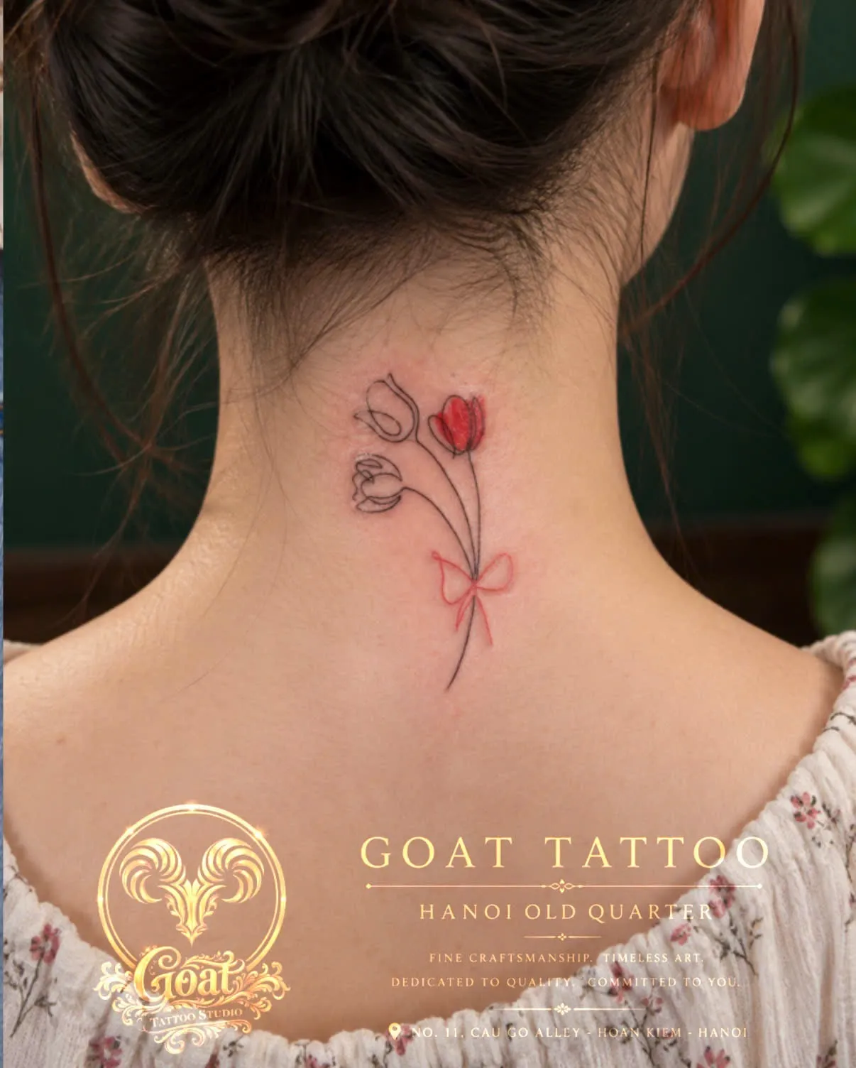 Fine line tulips with a red bow accent, tattooed on the nape of the neck, by GOAT Tattoo Studio in Hanoi's Old Quarter.