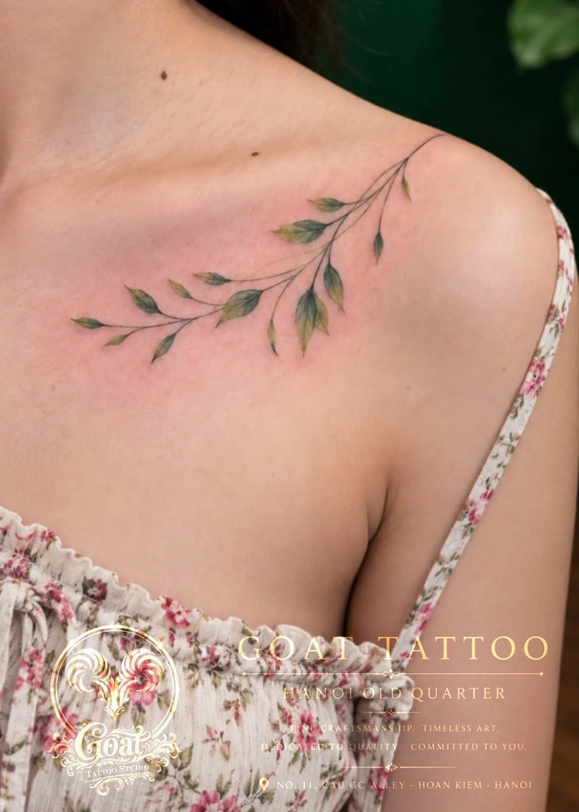 A trailing green vine branch tattoo across the collarbone and shoulder, by GOAT Tattoo Studio Hanoi.