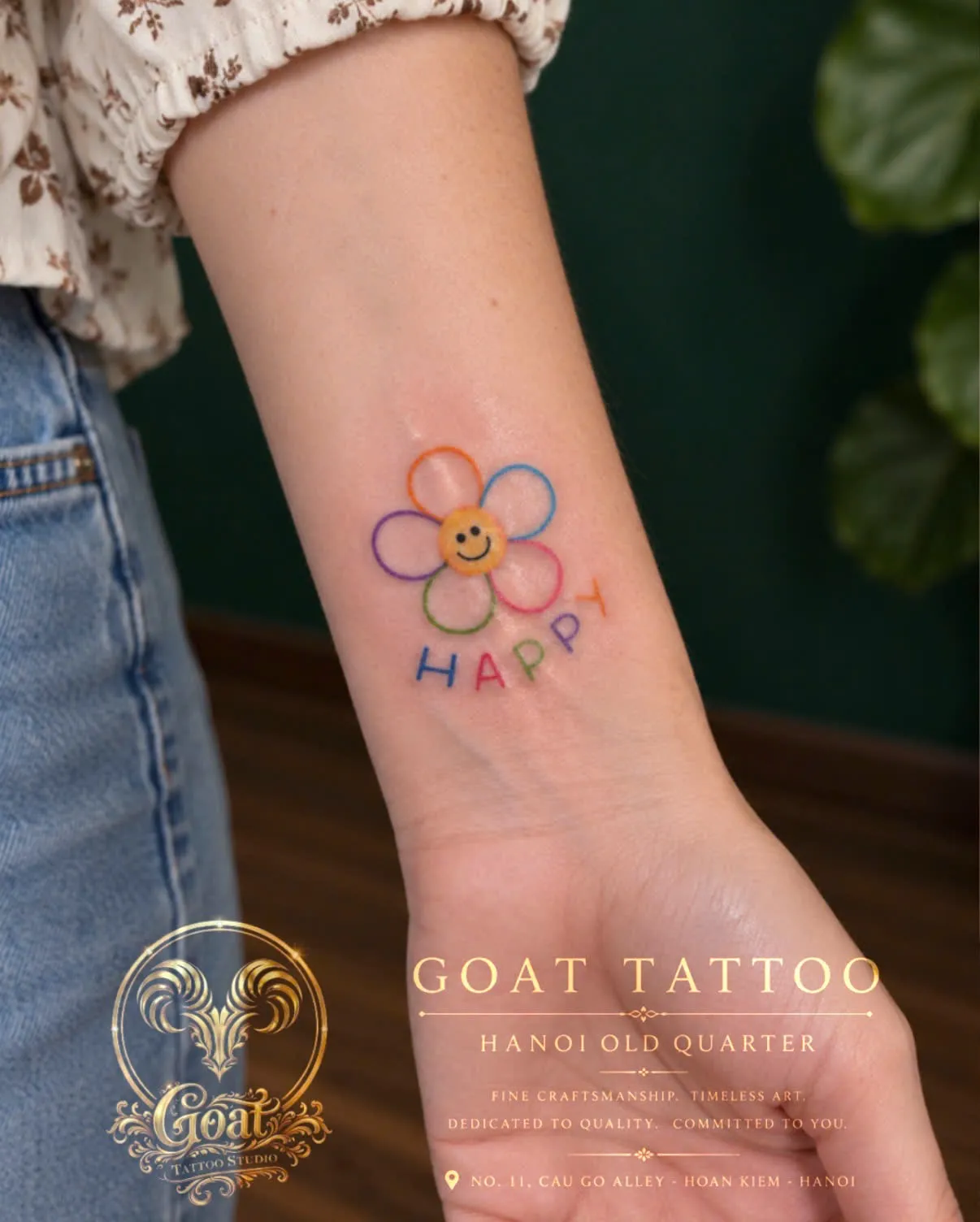 A colorful fine line daisy tattoo with a smiley face and the word Happy, on the wrist, by GOAT Tattoo Studio Hanoi.