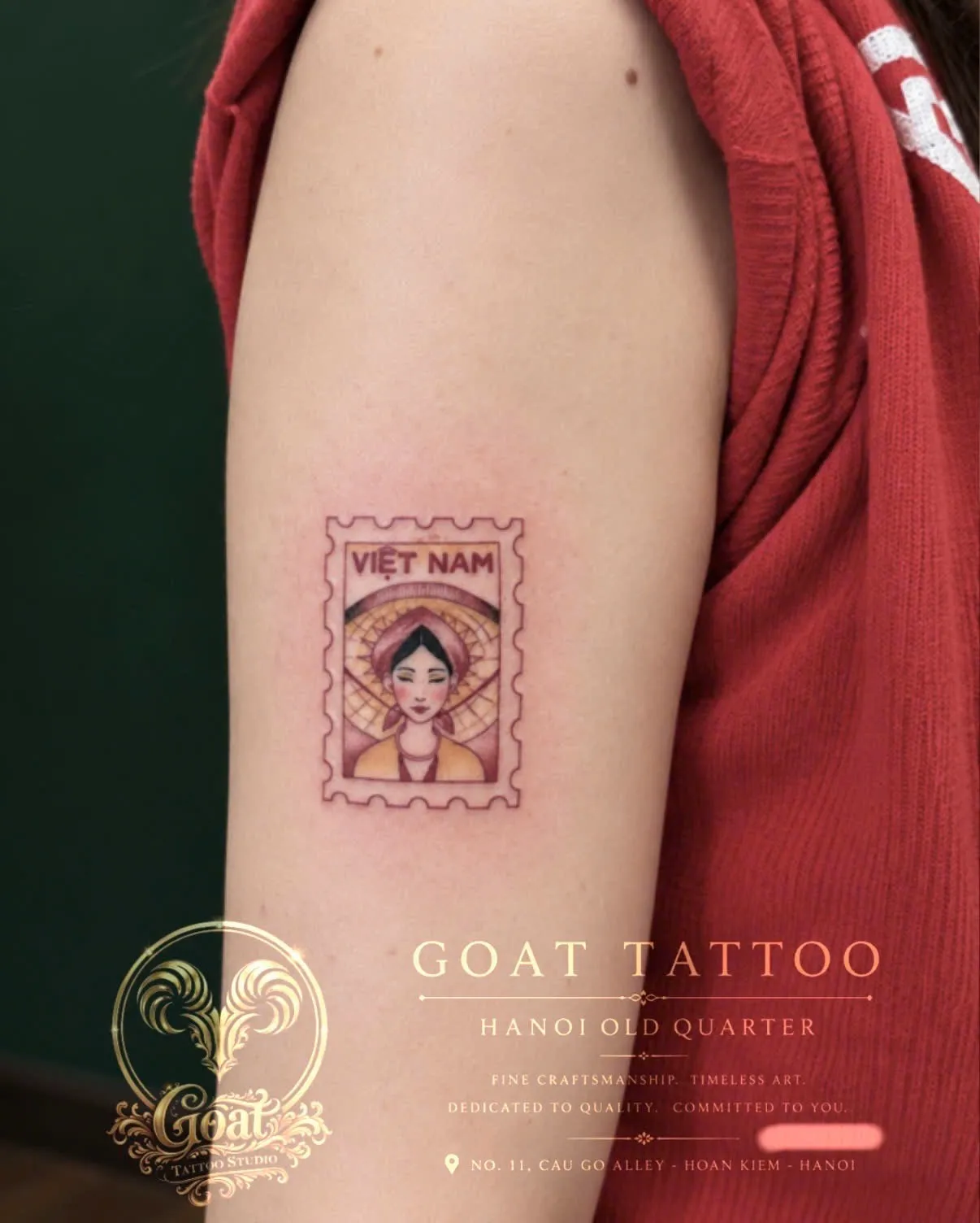 A colorful postage-stamp style tattoo of a Vietnamese woman in a conical hat, on the upper arm, by GOAT Tattoo Studio Hanoi.