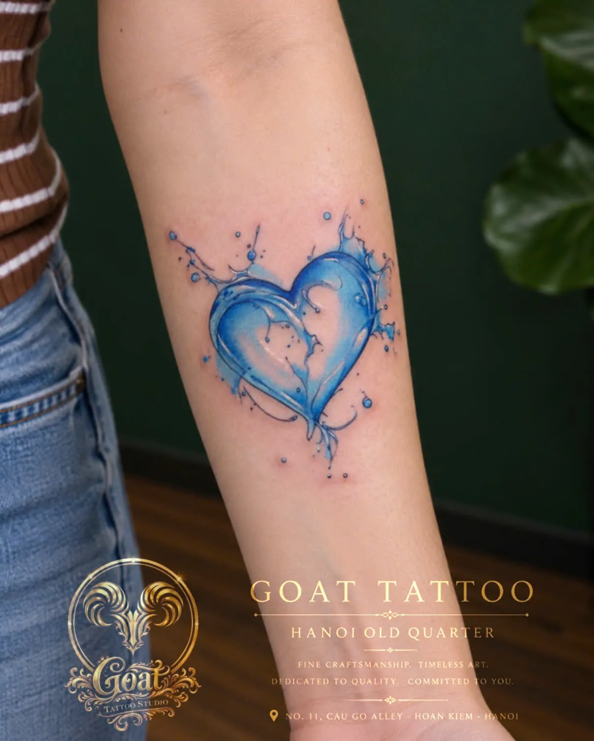 A blue watercolor-style splash heart tattoo on the forearm, by GOAT Tattoo Studio Hanoi.