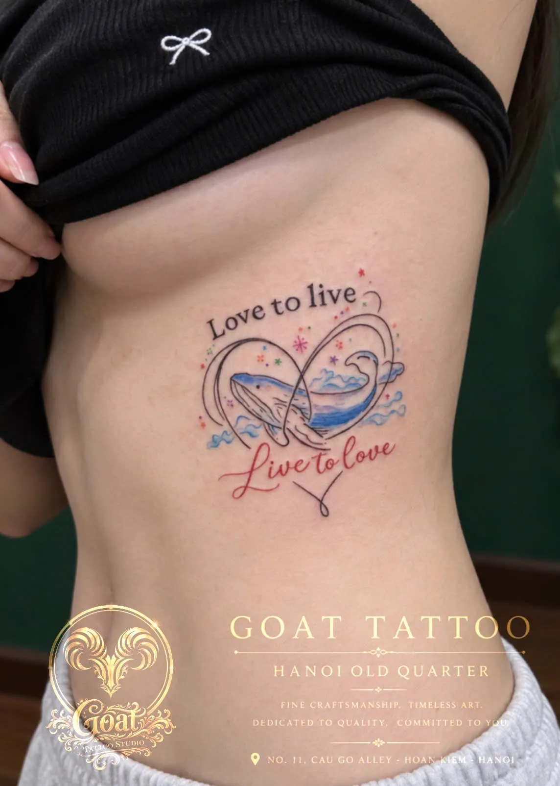 A colorful whale inside an infinity symbol with a Love to Live, Live to Love script, tattooed down the ribs, by GOAT Tattoo Studio in Hanoi's Old Quarter.